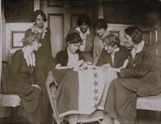 Alice Paul cousant des étoiles sur le drapeau du suffrage sous le regard d